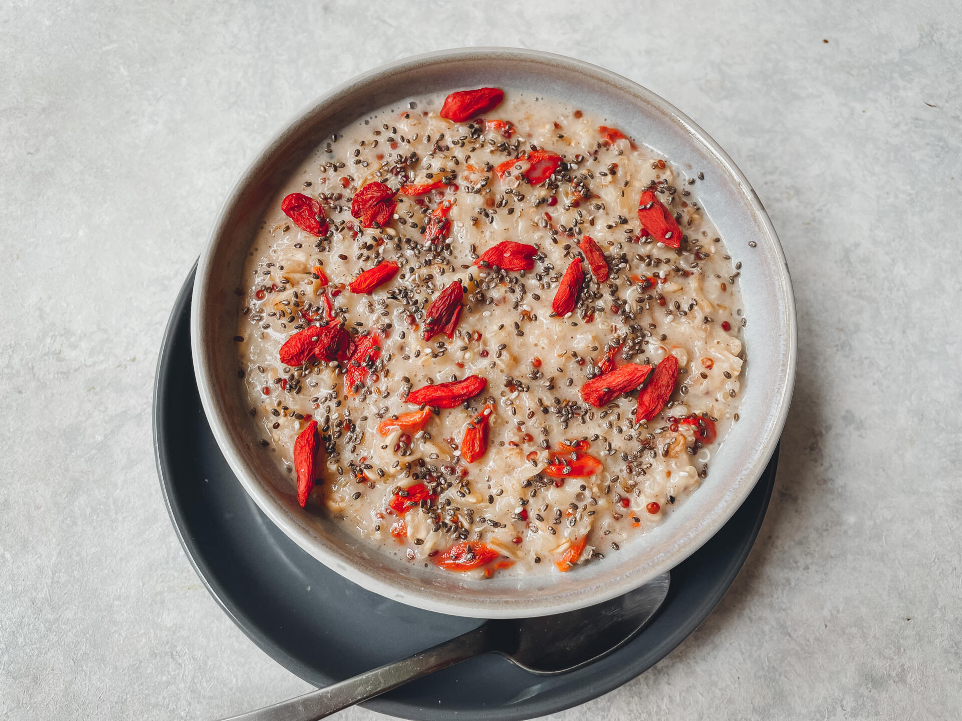 Grey bowl filled with quinoa, bulgur and oatmeal porridge with goji berries and chia seeds